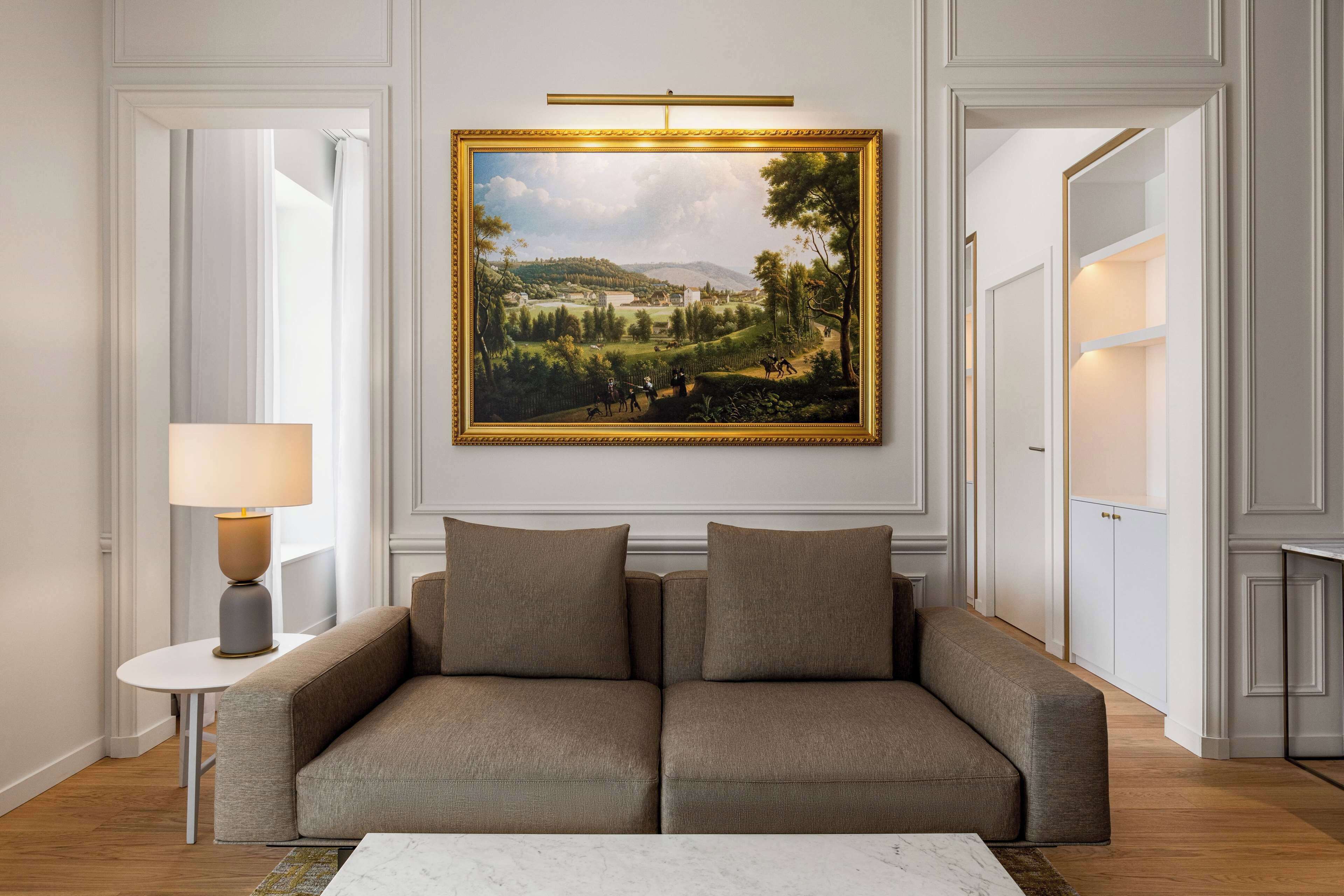 Un salon moderne avec un grand tableau représentant un paysage, un canapé, une table d’appoint et une lampe.