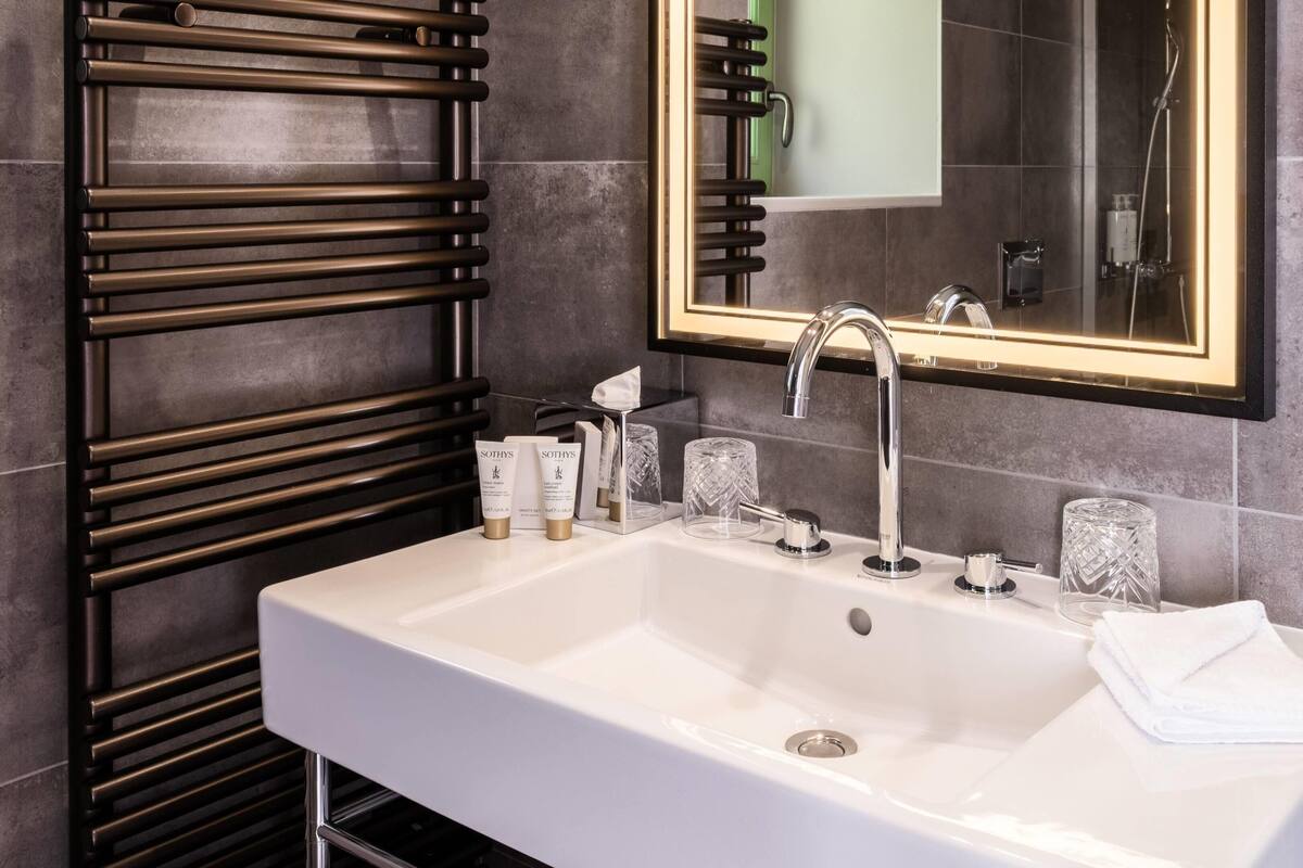 A modern bathroom with a white sink, a large mirror, and a towel rack.