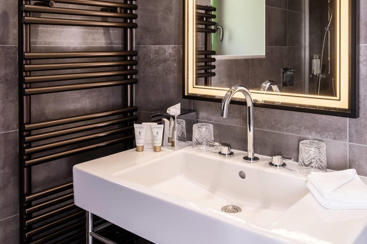 A modern bathroom with a white sink, a large mirror, and a towel rack.
