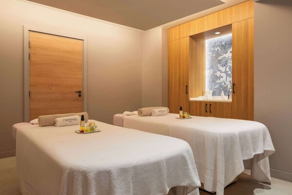 A room with two massage tables, each with a towel and a bottle of lotion.