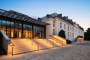 A hotel entrance with a glass facade, a covered outdoor area, and a set of stairs leading to the entrance. - Dolce By Wyndham Versailles - Domaine Du Montcel (Jouy-en-Josas)