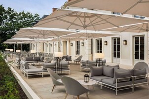 An outdoor seating area with multiple tables and chairs, large umbrellas, and ambient lighting.