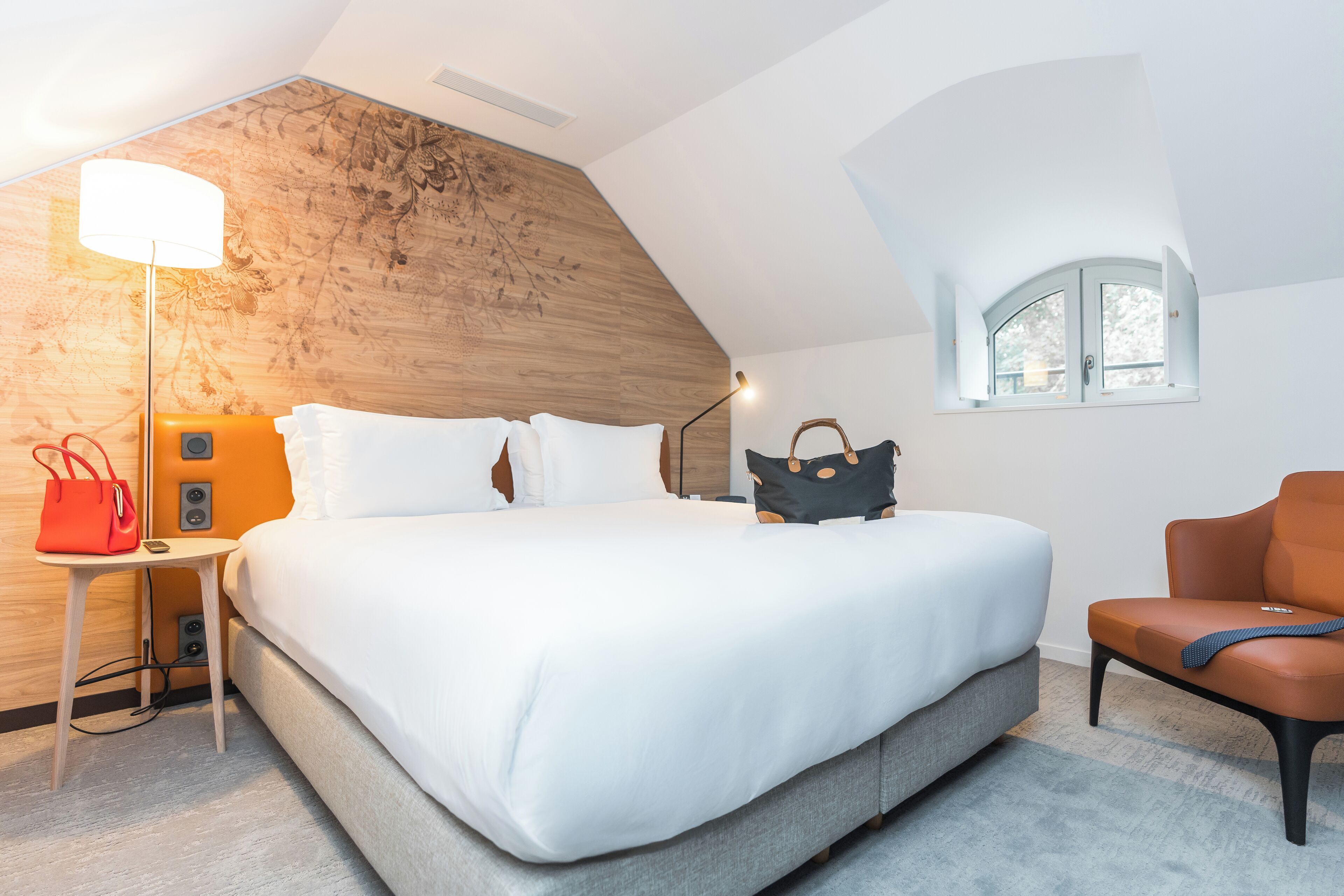 Ein modernes Schlafzimmer mit einem großen Bett, einem Nachttisch, einer Lampe, einem Sessel und einem Fenster.
