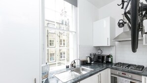 Een moderne keuken met een groot raam, witte kasten, een roestvrijstalen spoelbak en een gasfornuis.