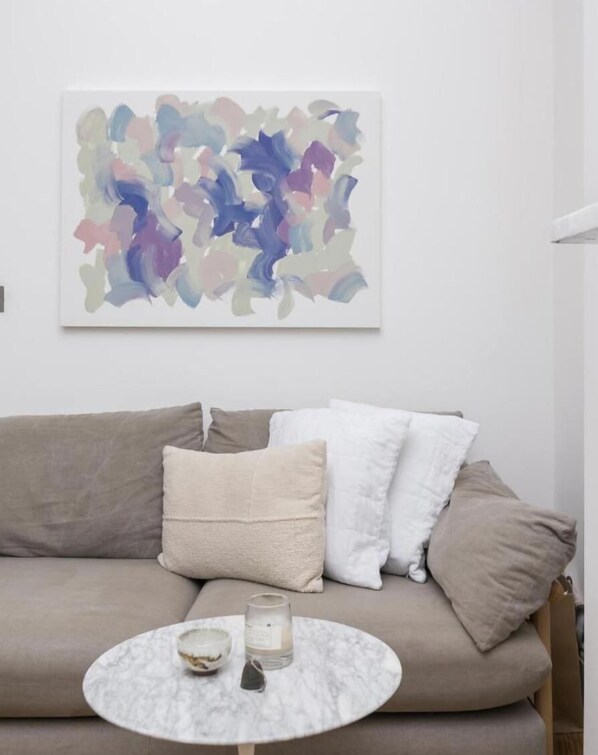 A living room with a beige sofa, a round marble coffee table, and a colorful abstract painting on the wall.