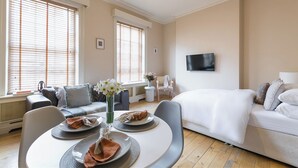 A modern hotel room with a bed, a dining area with a table set for two, and a seating area with a sofa and chairs. - Charming London City Apartment (London)