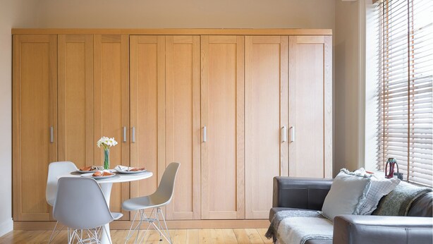 A room with a dining table, chairs, a sofa, and a large wooden wardrobe. - Charming London City Apartment (London)