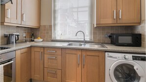 A modern kitchen with wooden cabinets, a stainless steel sink, a microwave, a kettle, and a washing machine. - Charming London City Apartment (London)