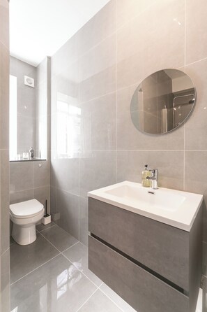 A modern bathroom with a white sink, a round mirror, and a toilet.