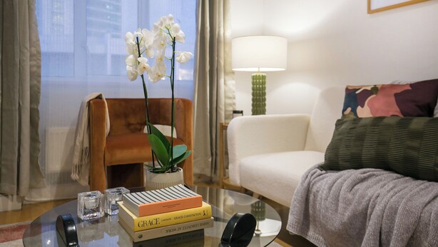 Une chambre d’hôtel avec une table basse en verre, un canapé blanc, une lampe verte et une fenêtre avec des rideaux.