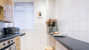 Une cuisine moderne avec des carreaux blancs, un four à micro-ondes, une machine à café et deux tabourets.