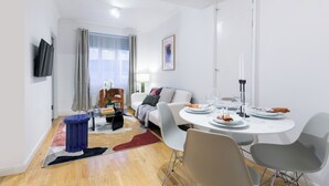 Un salon moderne avec un canapé, une table à manger pour deux personnes et un téléviseur fixé au mur.