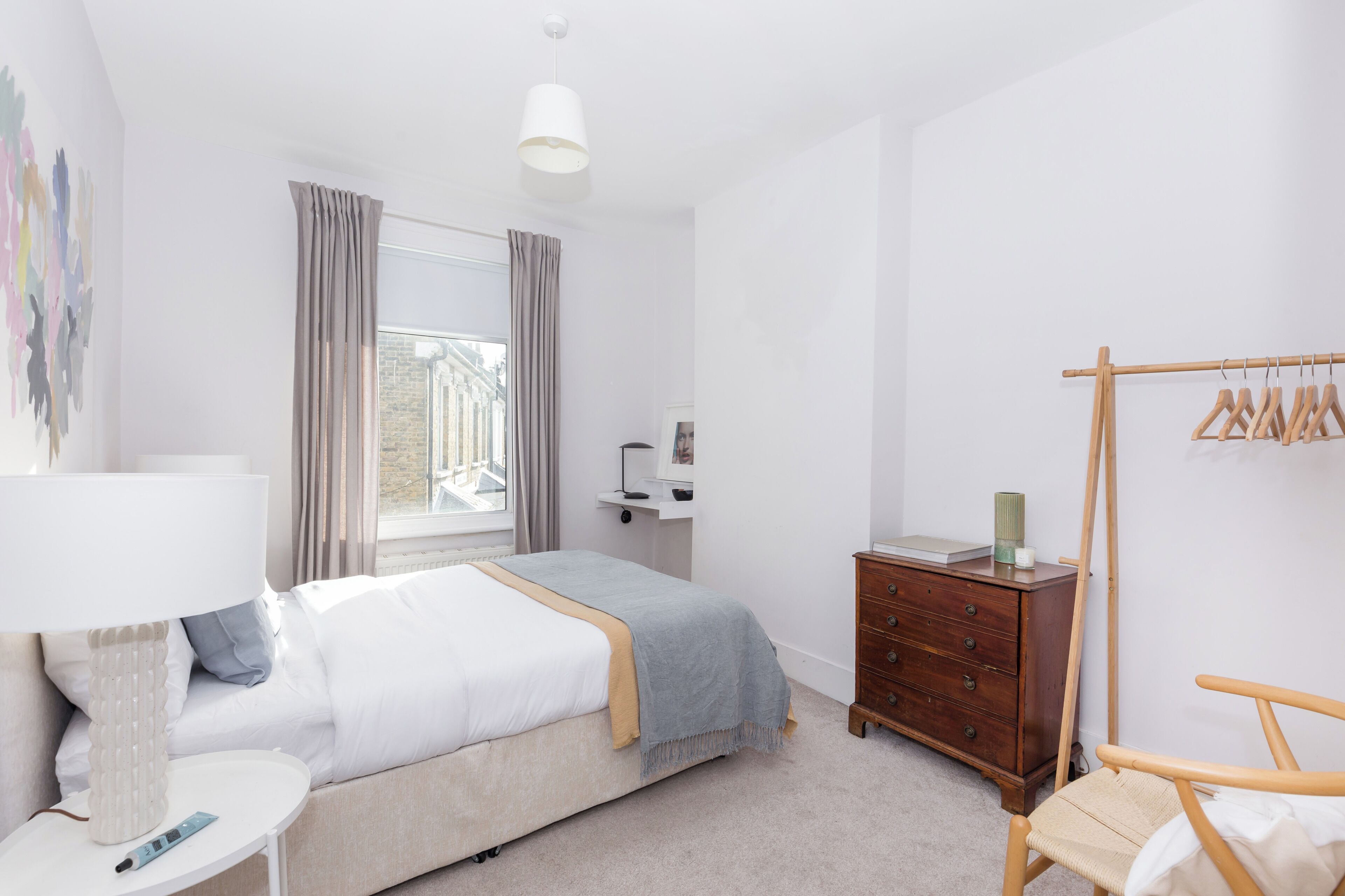 Une chambre à coucher comprenant un lit, une table de chevet, une lampe, une commode, une chaise et une fenêtre avec des rideaux.