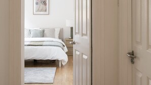 A bedroom with a bed, a nightstand, and a wall-mounted lamp. - Generously Large 1 Bedroom Apartment in Farringdon (London)