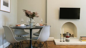 A dining area with a round table, four chairs, a vase with flowers, wine glasses, and a flat-screen TV mounted on the wall. - Chic 1 Bedroom Apartment in Bloomsbury (London)