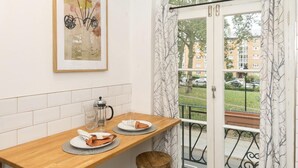 A kitchen with a wooden table, two stools, a hanging light fixture, a framed picture, and a view through a glass door. - Chic 1 Bedroom Apartment in Bloomsbury (London)