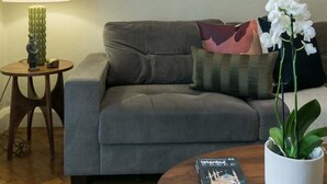 A living room with a grey sofa, a round wooden coffee table with a book and a potted plant, a floor lamp, and a framed artwork on the wall. - Chic 1 Bedroom Apartment in Bloomsbury (London)
