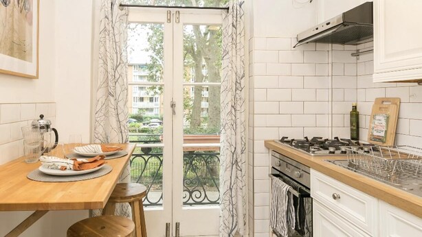 A kitchen with a wooden table, stools, a stove, and a view through a glass door. - Chic 1 Bedroom Apartment in Bloomsbury (London)