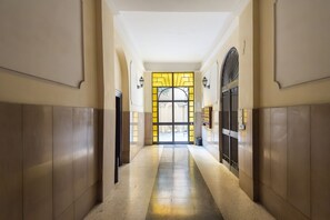 Un couloir doté d’un sol carrelé, d’une porte en verre agrémentée de touches de couleur jaune et d’un portail en métal.