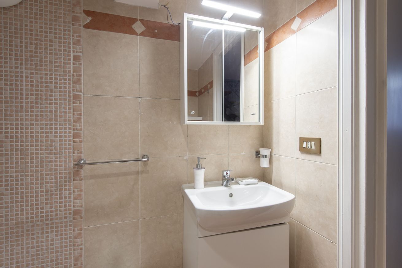 A bathroom with a tiled floor, a sink with a mirror above it, and a towel rack.