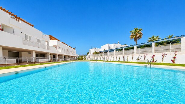 A swimming pool with clear blue water, surrounded by white buildings with balconies and a palm tree. - AlmeriaSuite Mojacar Breeze Sun101 (Mojacar)