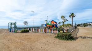 Une plage de sable avec une aire de jeux colorée et un palmier.
