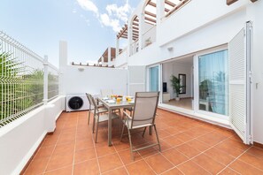 A patio with a table and chairs, a white wall, and a sliding glass door. - AlmeriaSuite Mojacar Breeze Sun108 (Mojacar)