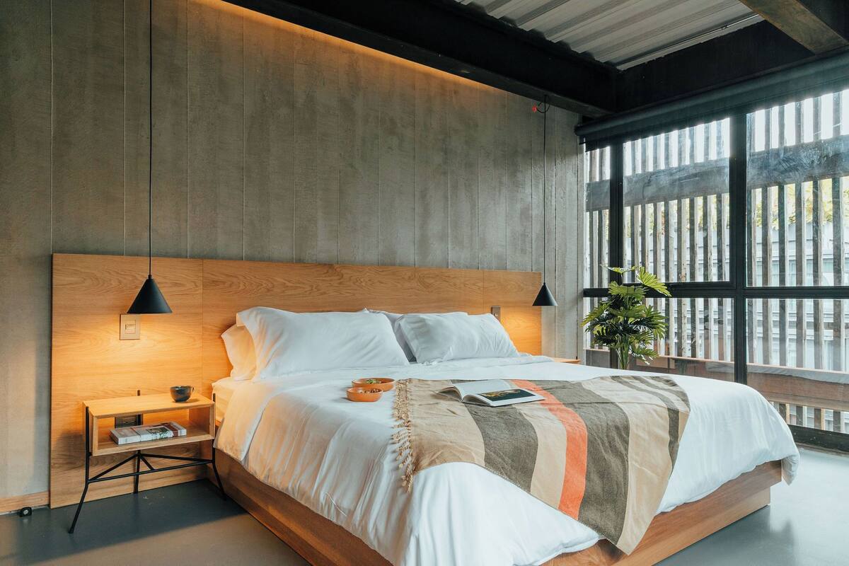A modern bedroom with a large bed, wooden headboard, bedside tables, and a window with a view.