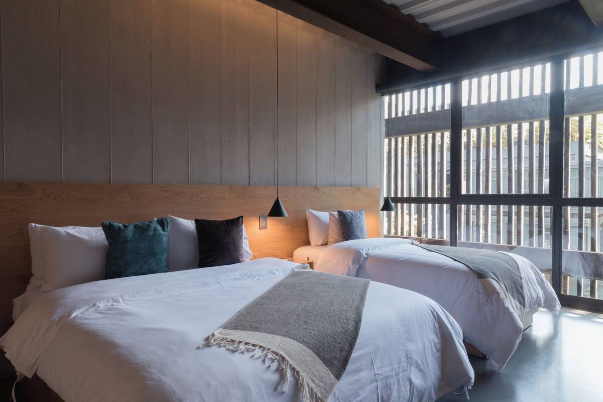 A hotel room with two beds, wooden paneling on the walls, and a large window with a view of the outside.