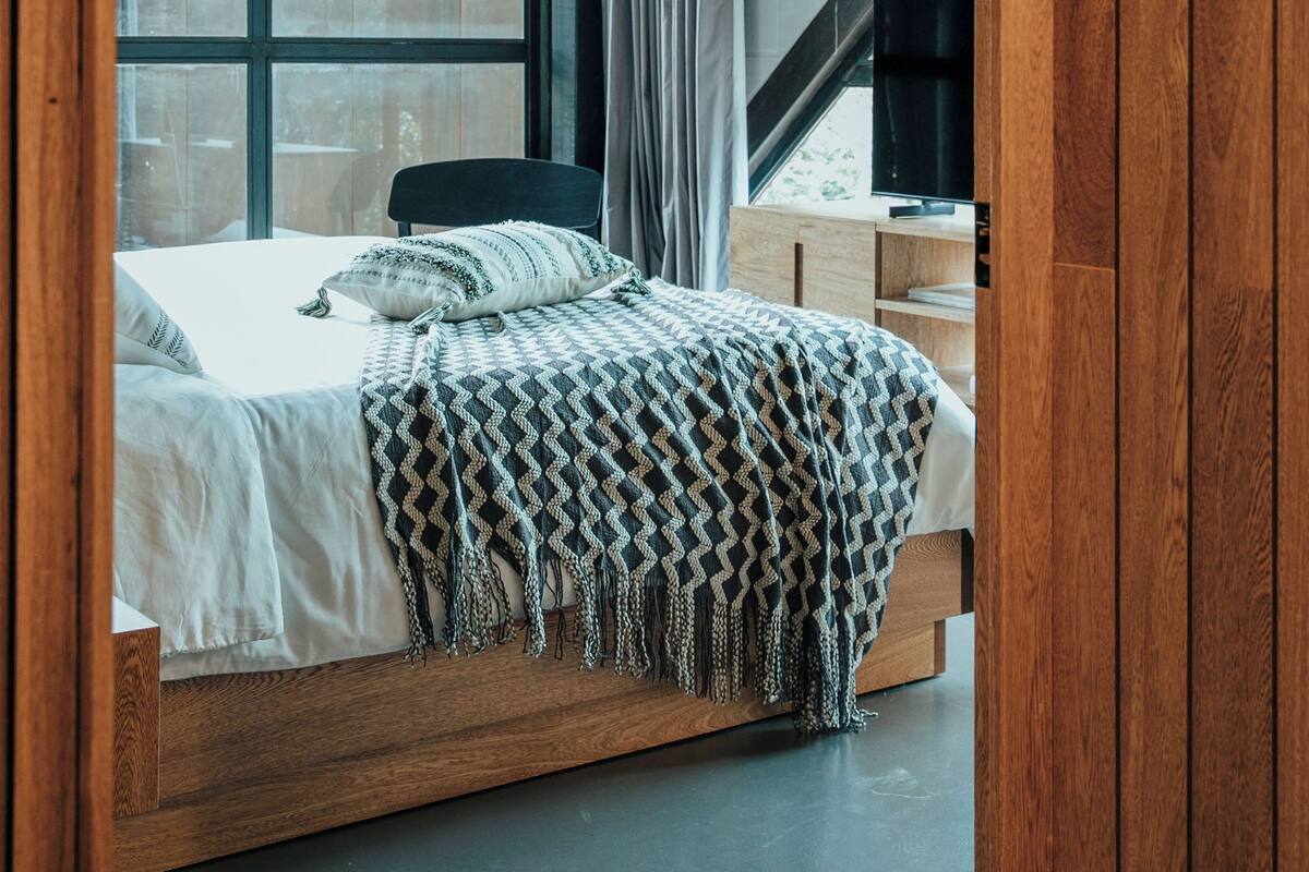 A bedroom with a large window, a bed with a patterned blanket, and a view of a staircase.