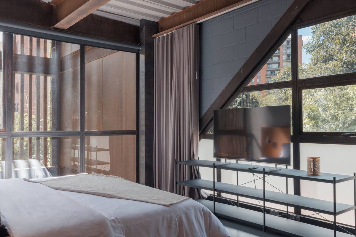 A modern hotel room with a large bed, a TV, and a balcony with a view of the city.