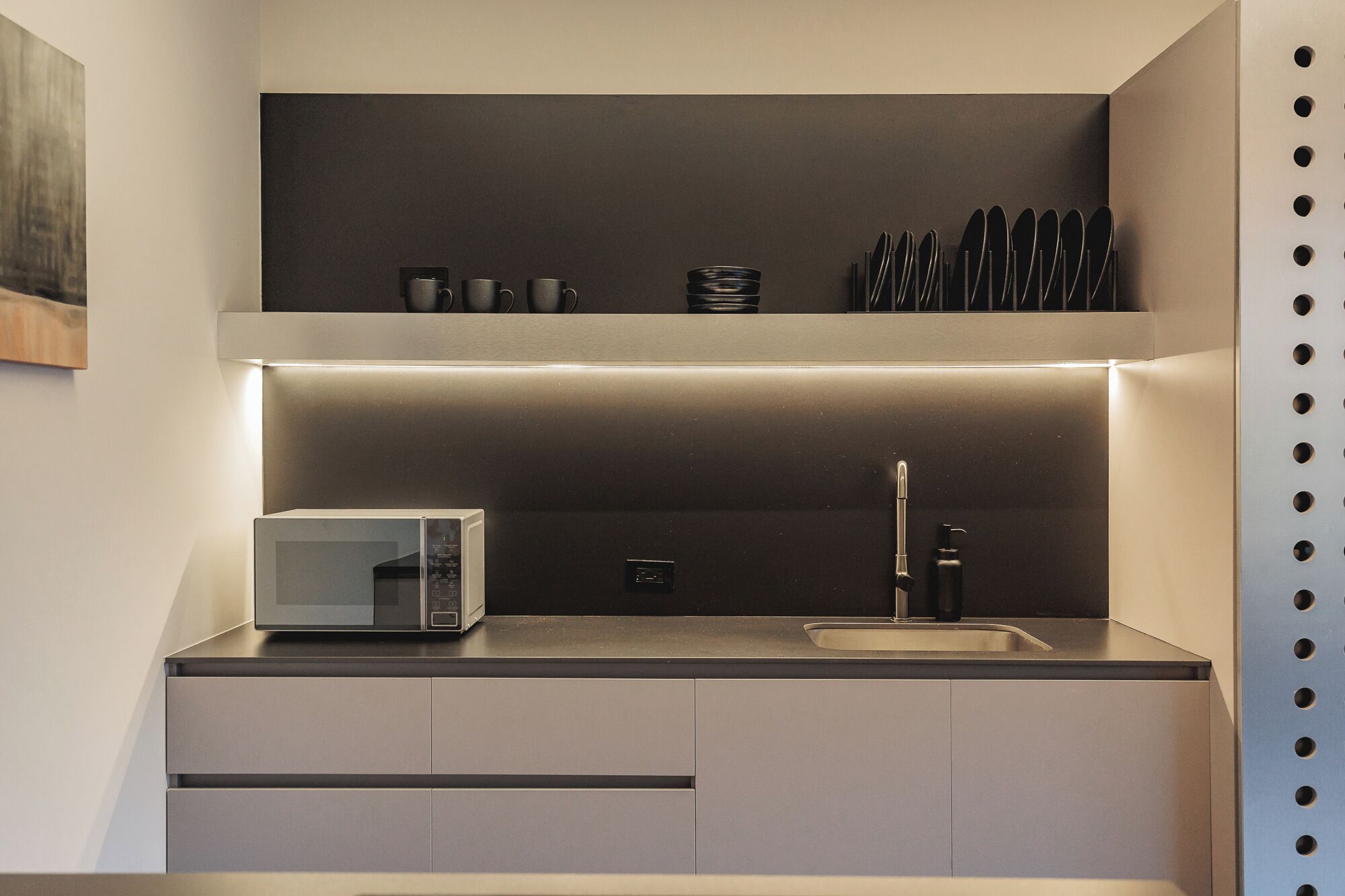 A compact kitchen with a microwave, sink, and utensil holder.