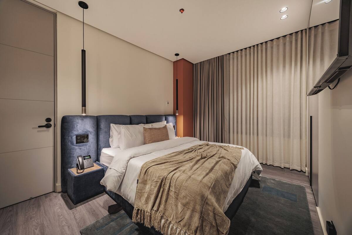 A modern hotel room with a large bed, a bedside table with a phone, and a window with curtains.
