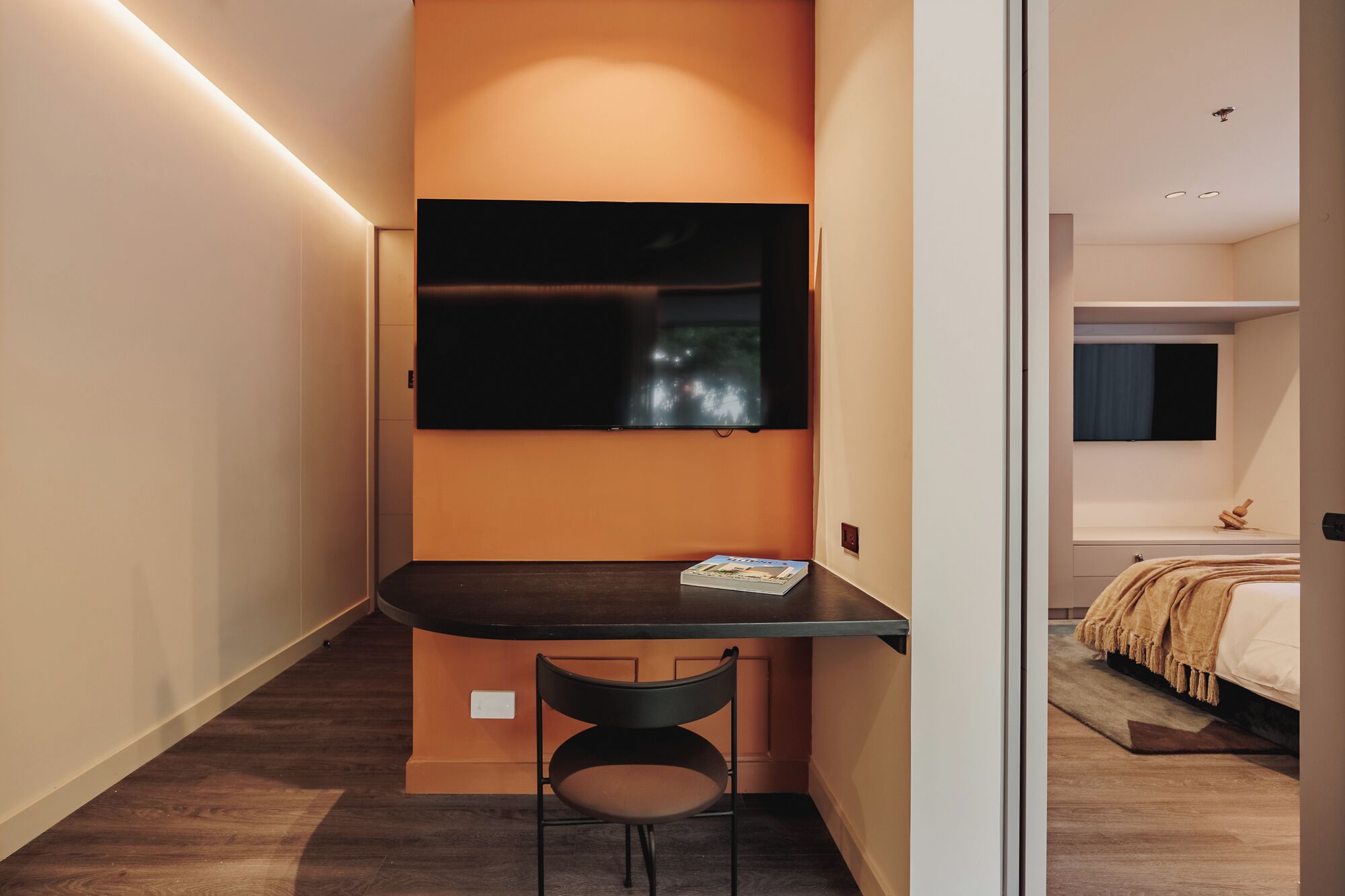 A compact bedroom with a bed, a desk, and a TV.