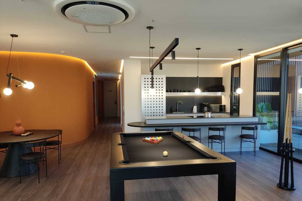 A modern kitchen with a pool table, bar area, and a dining space with a round table and chairs.