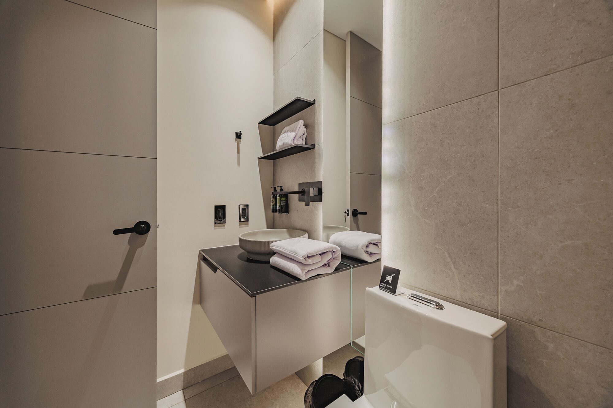 A modern bathroom with a round sink, a towel rack, and a toilet.
