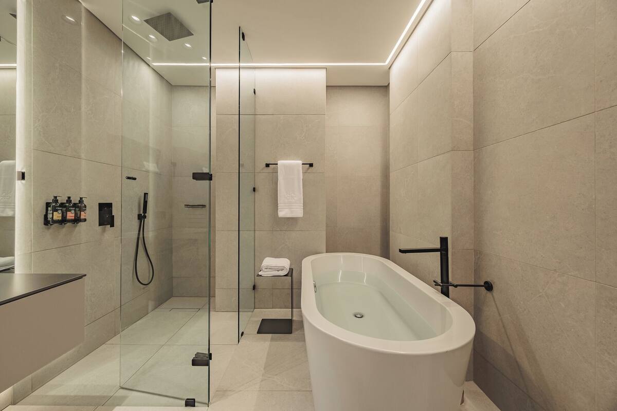A modern bathroom with a glass-enclosed shower, a freestanding bathtub, and a vanity with toiletries.