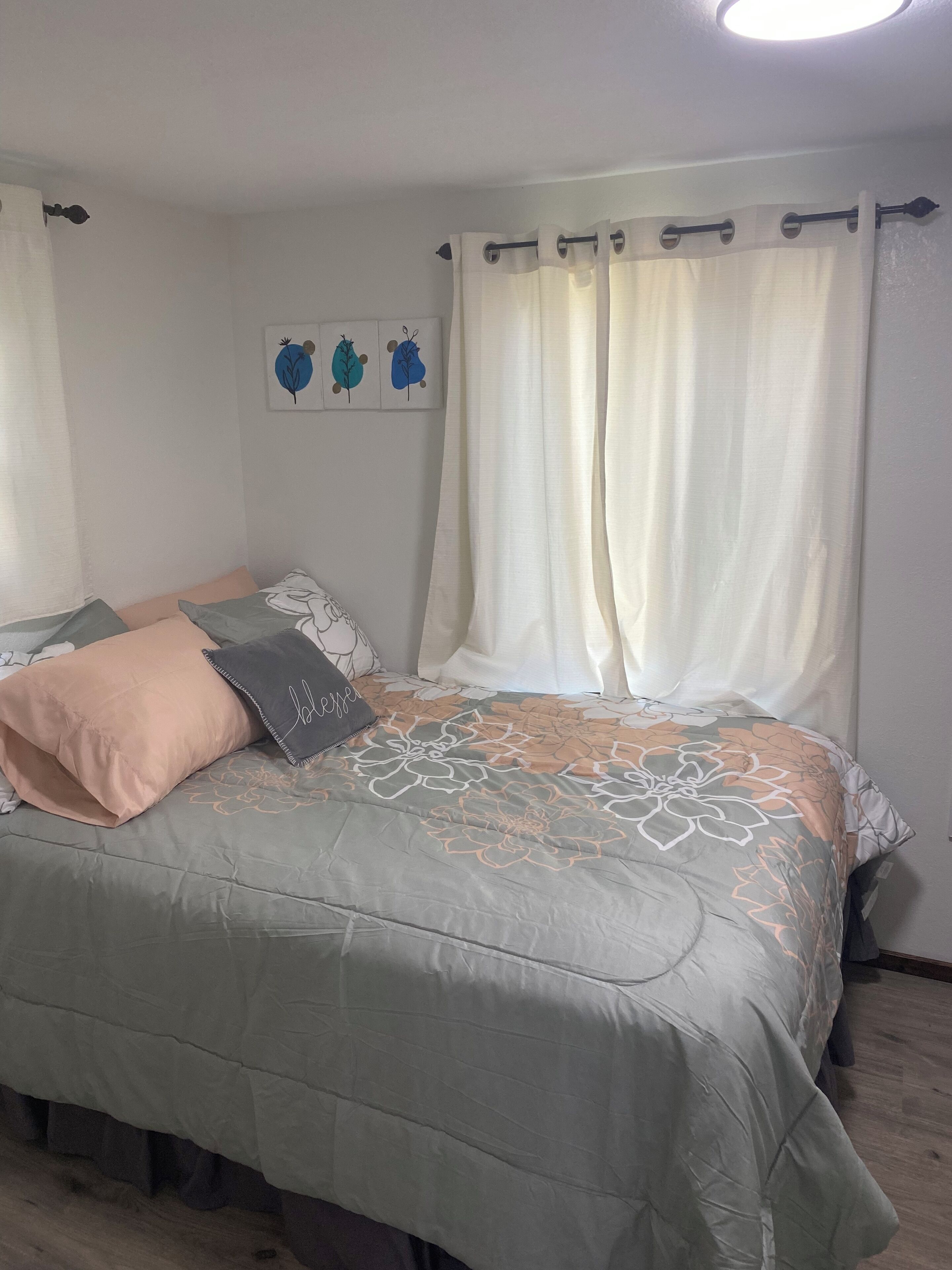 A bedroom with a bed, pillows, a wall-mounted artwork, and a window with curtains.