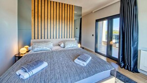 Quarto moderno com cama grande, ripas de madeira na parede e vista para o exterior através de uma porta de correr.