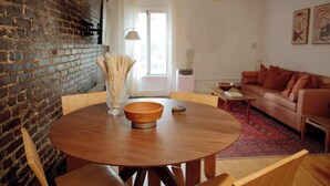 Een eetgedeelte met een ronde houten tafel, stoelen en een vaas met gedroogde planten.