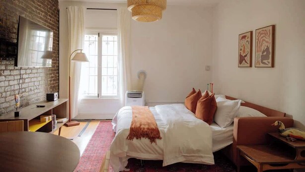 Een slaapkamer met een bed, een bureau, een stoel, een hanglamp en kunstwerken aan de muur.