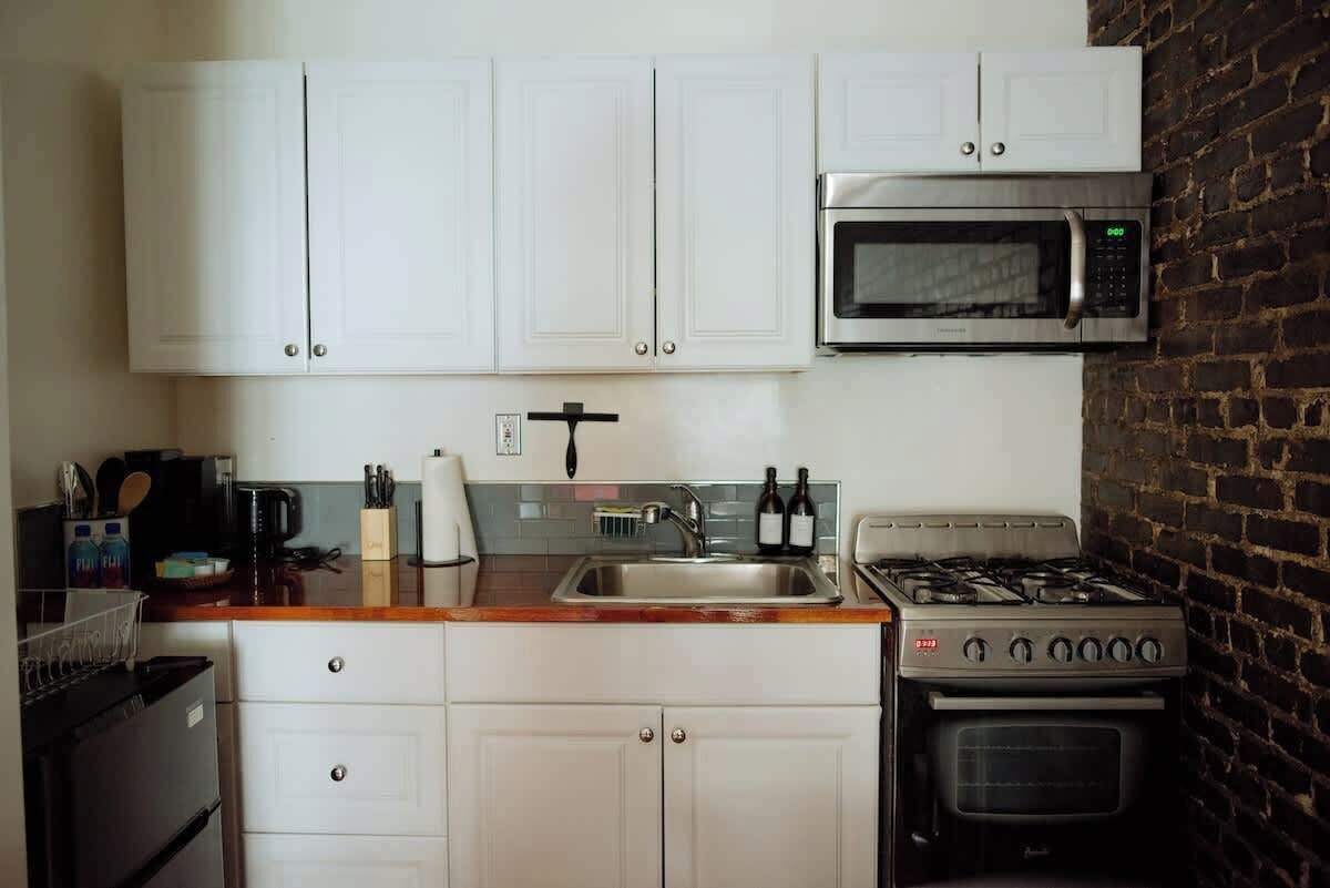 Una cucina compatta con mobili bianchi, un microonde in acciaio inossidabile, un piano cottura a gas e un forno integrato.
