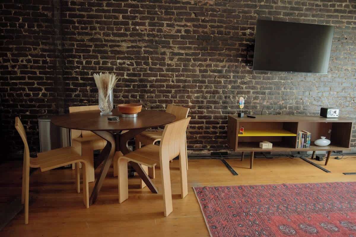 Een eetgedeelte met een bakstenen muur, een ronde houten tafel en stoelen.