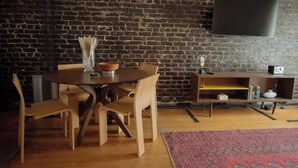 Een eetgedeelte met een bakstenen muur, een ronde houten tafel en stoelen.