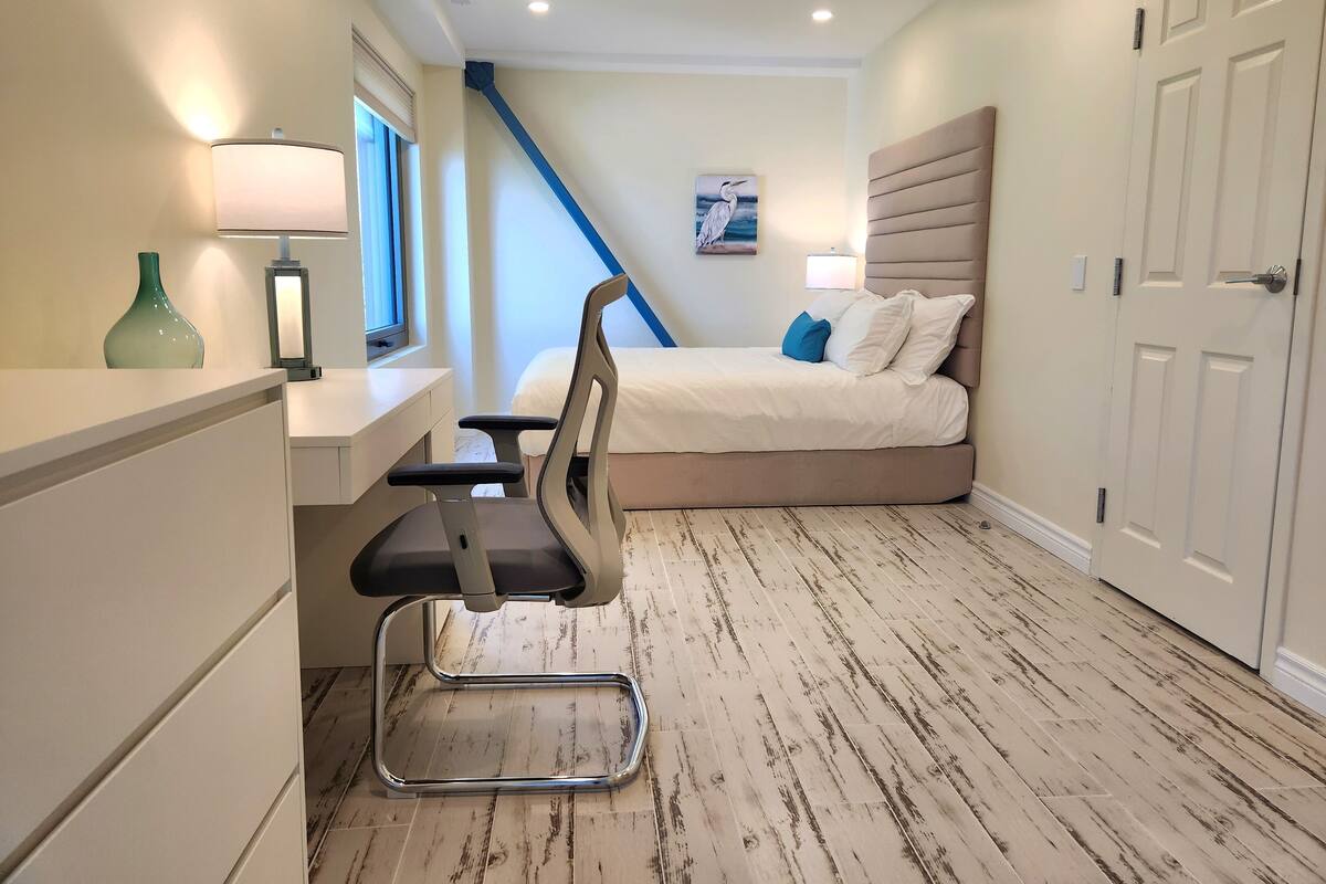A bedroom with a bed, desk, chair, and a window.