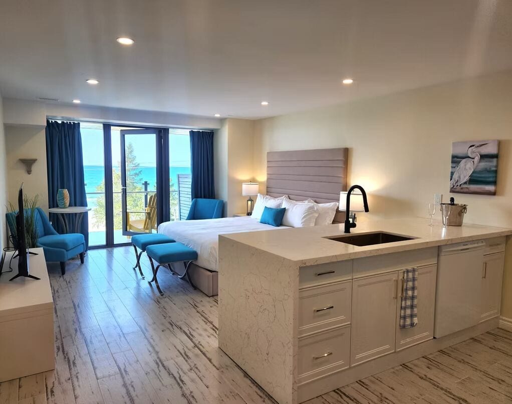 A hotel room with a bed, a small seating area, a kitchen island, and a view of the ocean.