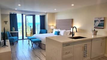 A hotel room with a bed, a small seating area, a kitchen island, and a view of the ocean.
