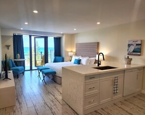 A hotel room with a bed, a small seating area, a kitchen island, and a view of the ocean. - The Sands (Sauble Beach)