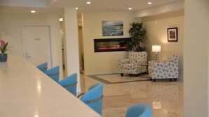 A dining area with a long table and blue chairs, a fireplace, and two patterned armchairs. - The Sands (Sauble Beach)