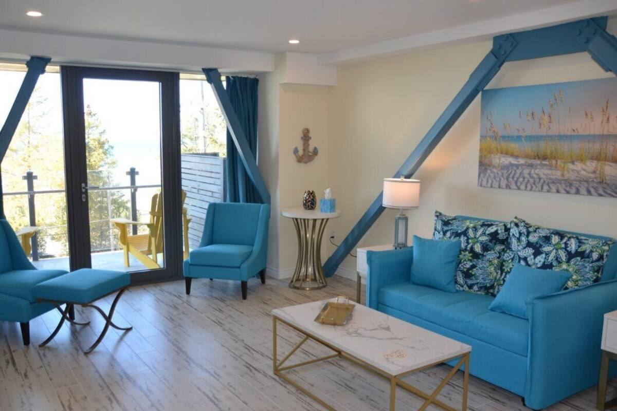 A living room with a blue sofa, matching armchair, and a coffee table. There is a painting on the wall and a lamp on a side table.